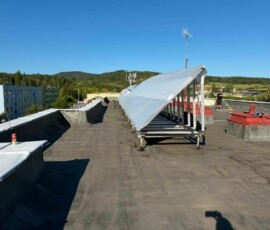 Původní hydroizolace ploché střechy bytového domu (535 m²) s konstrukcí pro solární panely. • Stará plochá střecha bytového domu s asfaltovými pásy a konstrukcí pro fotovoltaiku před zateplením PUR pěnou.