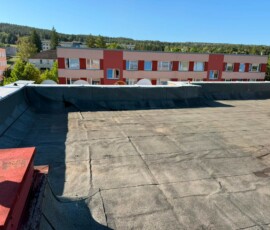 Původní stav hydroizolace ploché střechy bytového domu • Stará plochá střecha bytového domu s asfaltovými pásy a konstrukcí pro fotovoltaiku před zateplením PUR pěnou.